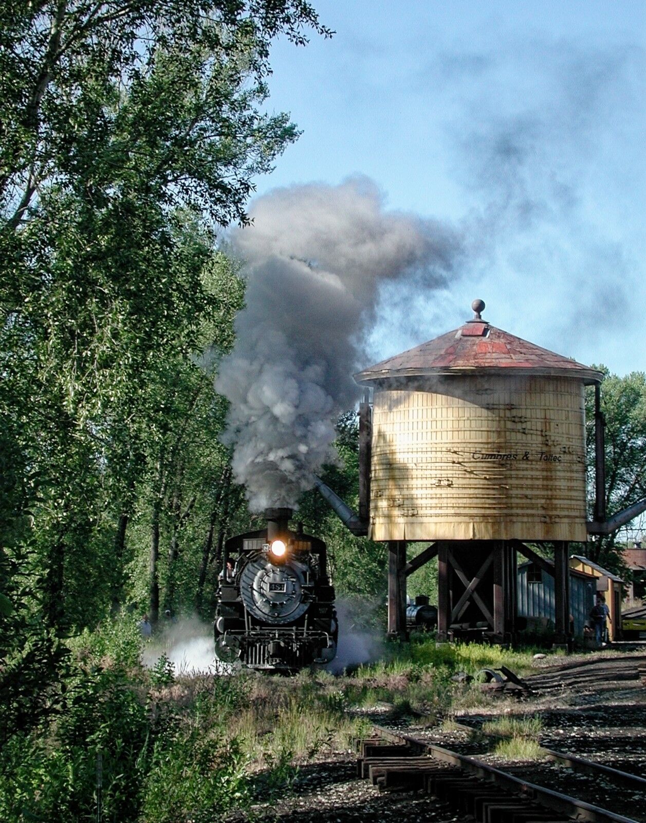 Morning sunshine at the double spout water tank in Chama New Mexico. The railfans watch in amazement as narrow gauge steam locomotive...