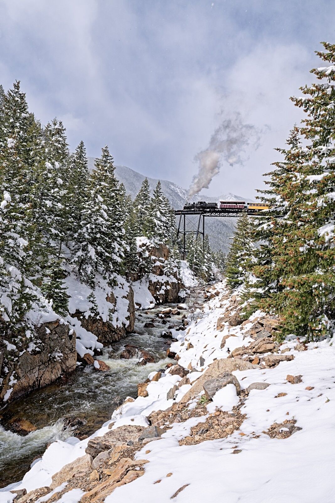 A heavy spring snow blankets the trees as a Silver Plume bound train crosses Devils Gate Bridge.