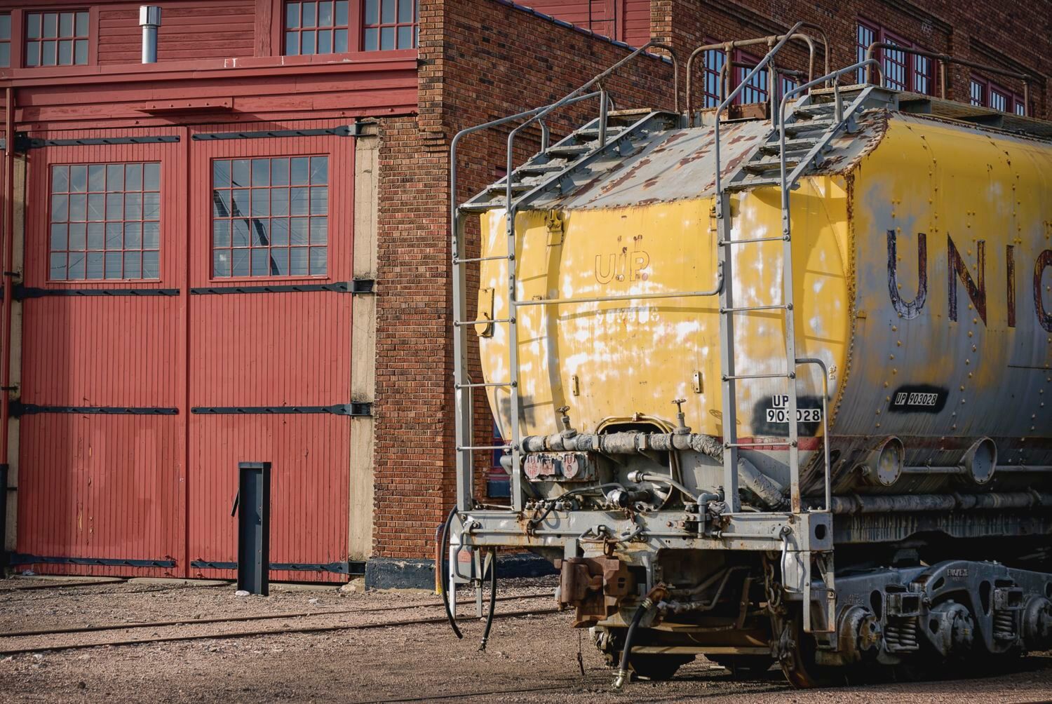 A steam locomotive tender and then a UP turbine tender is parked outside the roundhouse in Cheyenne Wyo.